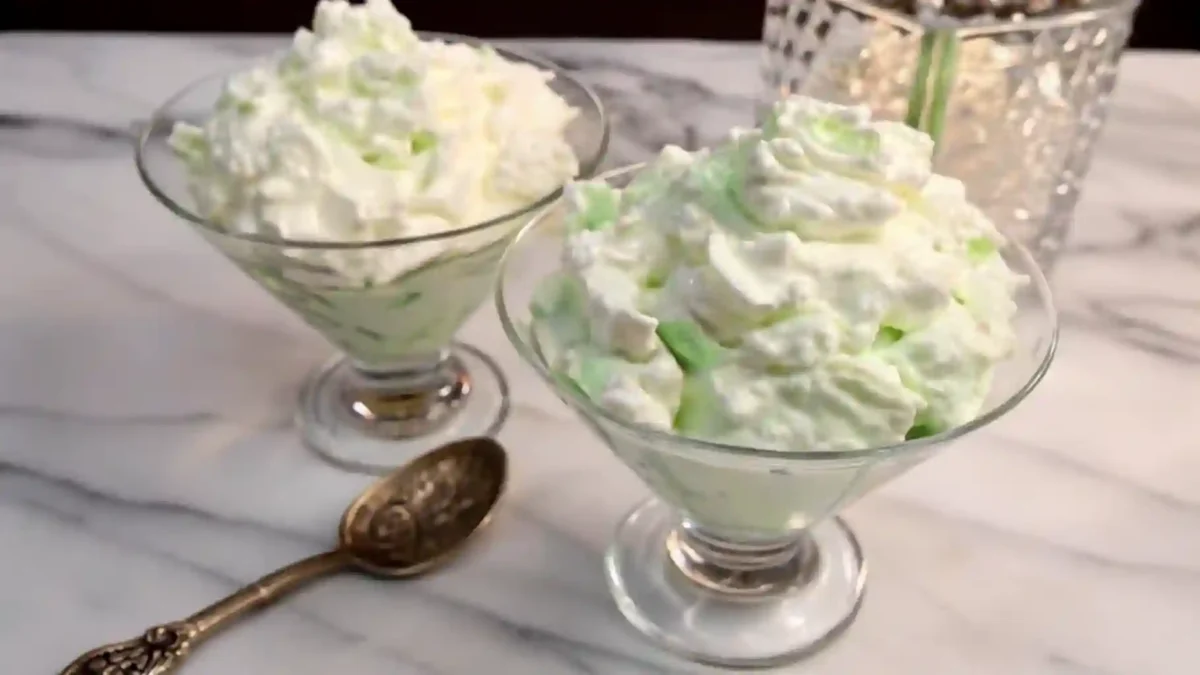 A creamy green pistachio salad served in a glass bowl, garnished with chopped pistachios and maraschino cherries, showcasing its fluffy texture and retro charm