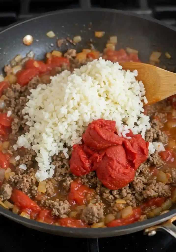Ground beef, onions, garlic, and tomatoes cooking in a skillet