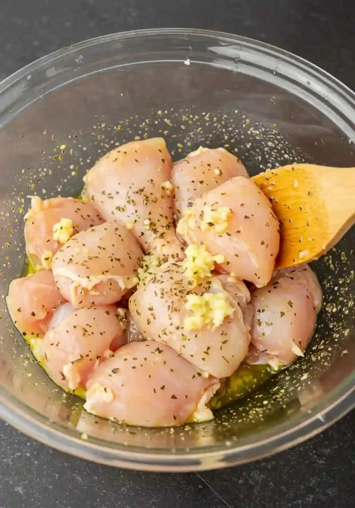 Chicken pieces in marinade with olive oil, lemon juice, and seasoning in a mixing bowl