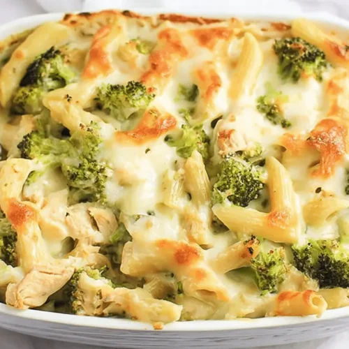 A creamy, baked chicken ziti broccoli alfredo casserole in a white baking dish with golden-brown melted cheese, penne pasta, and bright green broccoli florets, ready to be served.