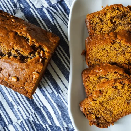 The Best Pumpkin Banana Bread Recipe for Fall Baking Freshly baked pumpkin banana bread loaf with chopped nuts and four ready-to-eat slices on a white plate.